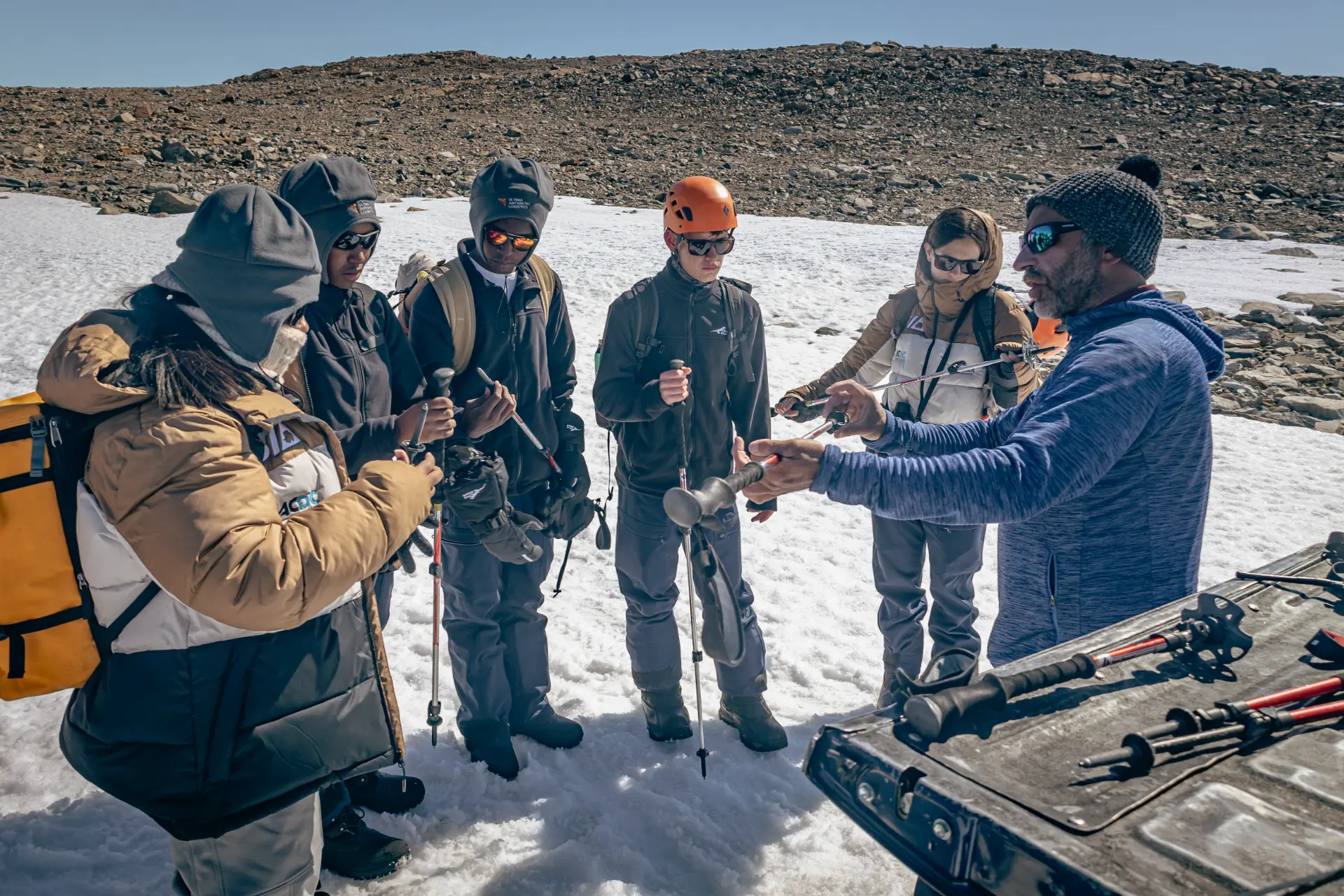 An instructor demonstrates trekking pole technique to students on a snowy slope