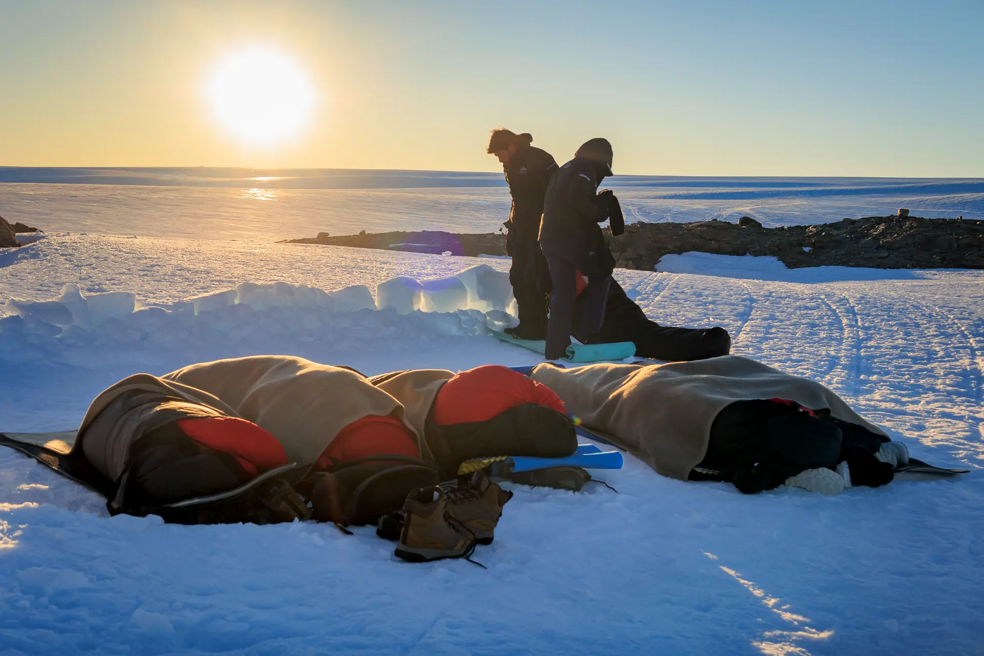 Students resting in sleeping bags on the snow at sunset near Ultima Base