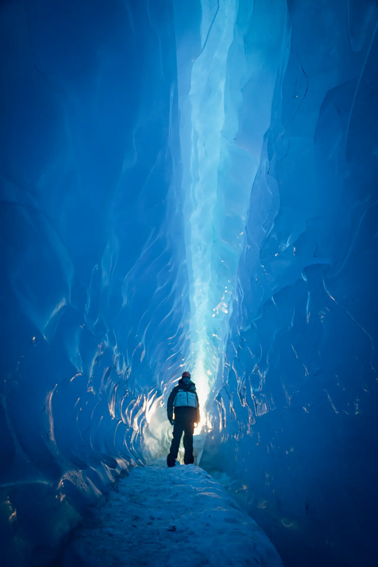 A lone figure standing inside a towering blue ice canyon in Antarctica
