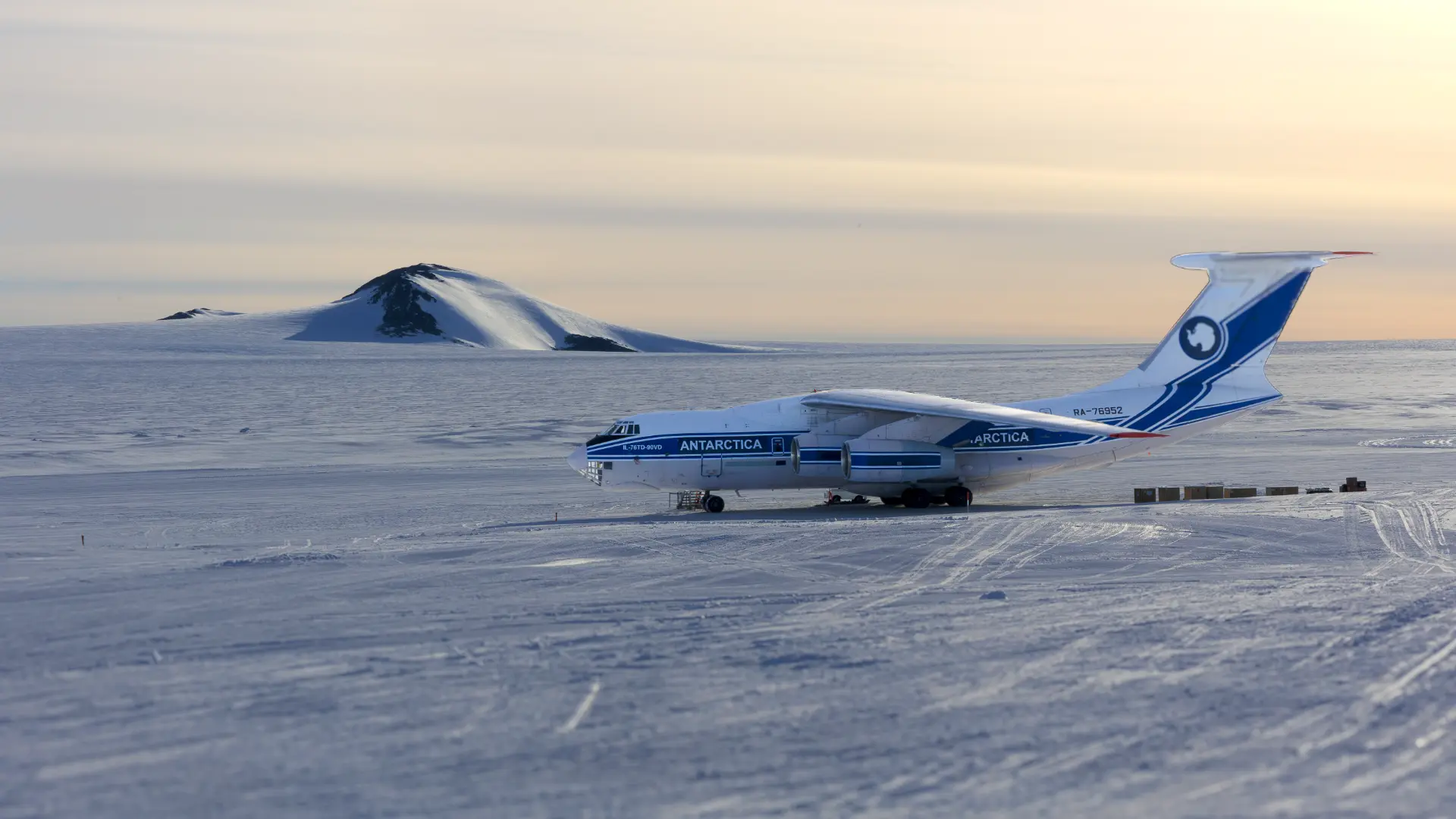 Ilyushin IL-76 aircraft marked Antarctica parked on a blue ice runway with a snow covered peak behind