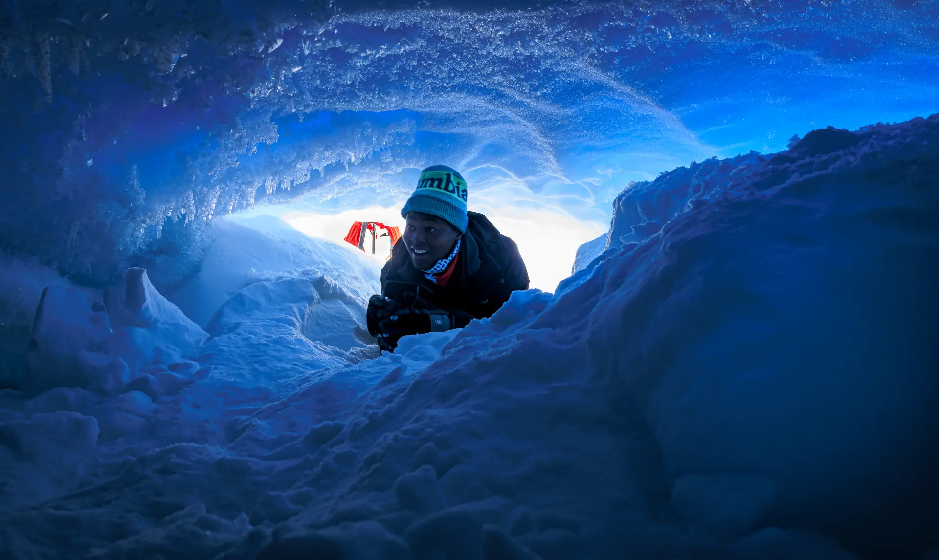 An expedition member emerging from a vivid blue ice cave