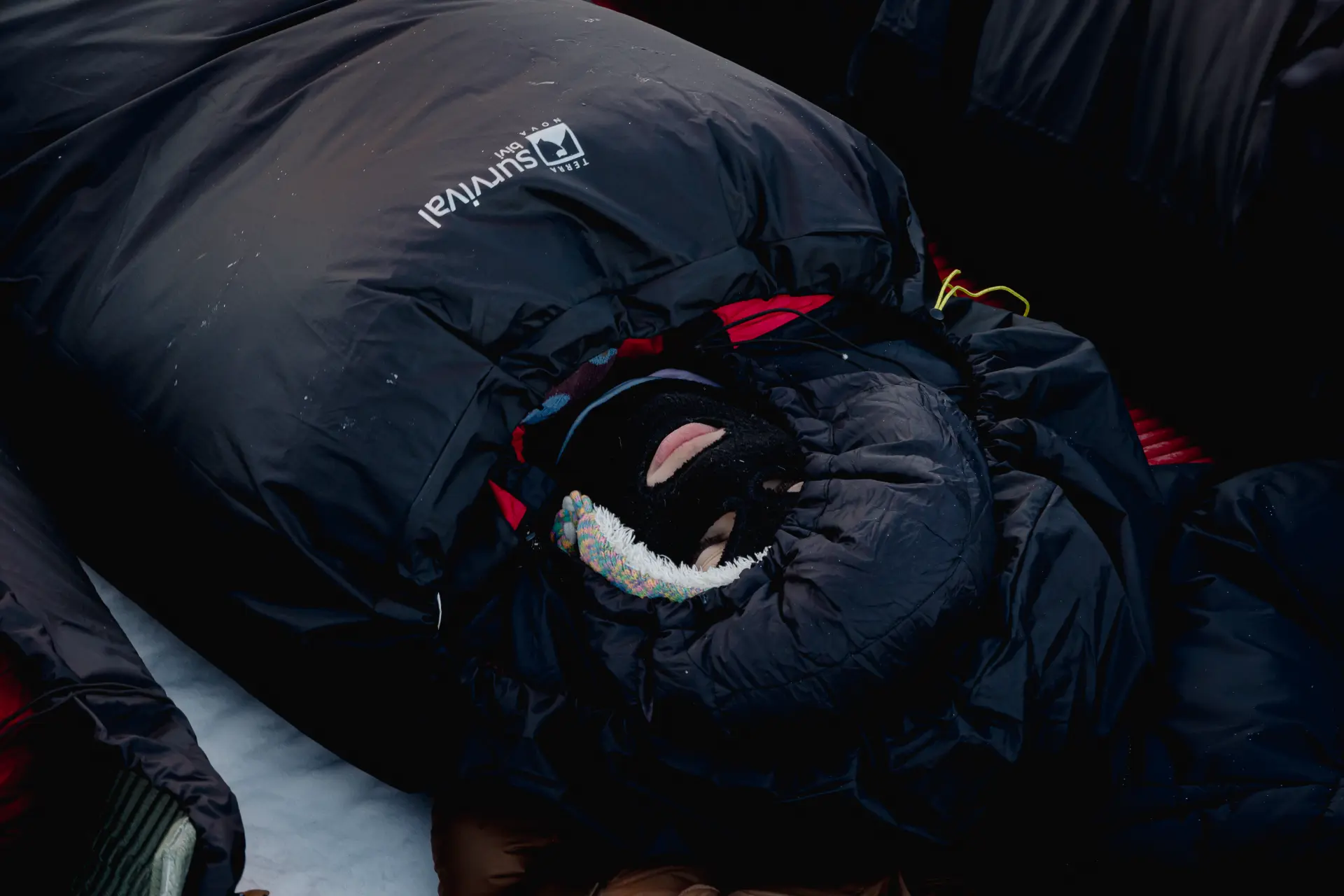 An expedition member resting inside a survival bivy bag on the snow at night