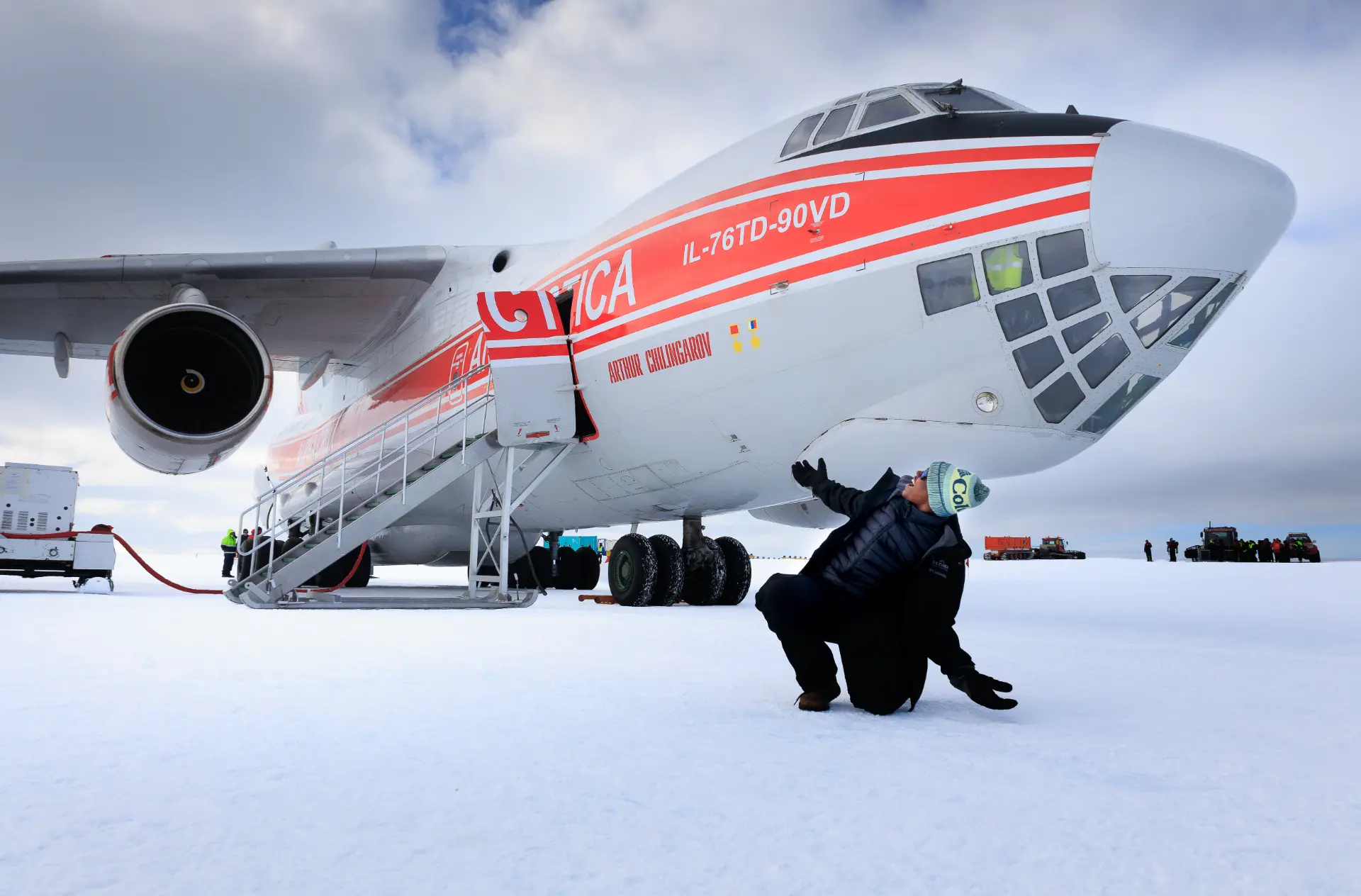 A student kneeling beneath the nose of the IL-76 cargo aircraft on the Antarctic ice runway