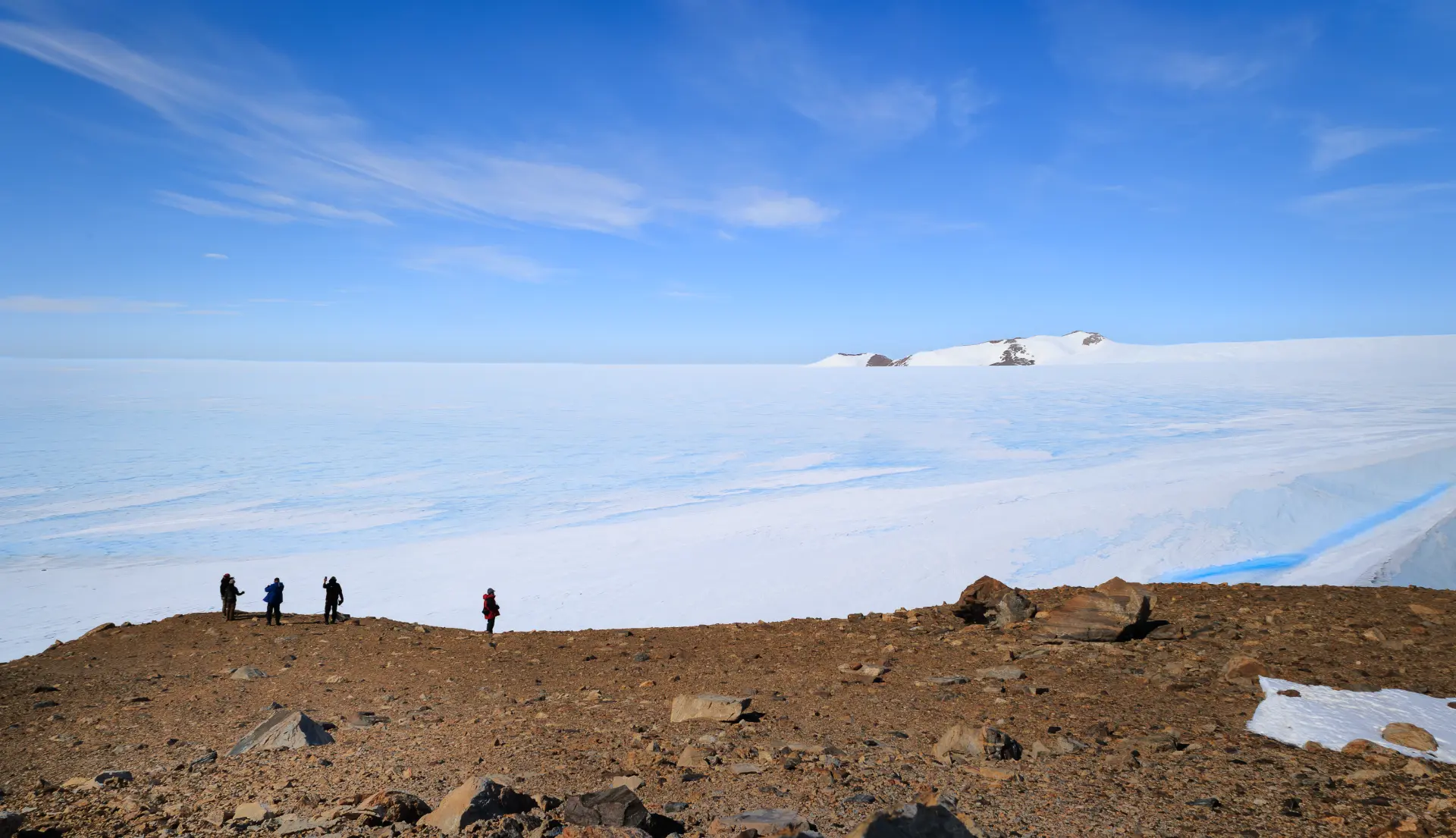 Four expedition members standing on a rocky ridge looking out over the Antarctic ice sheet
