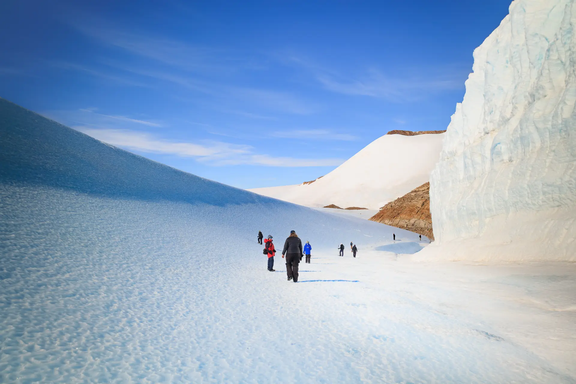 Expedition members walking across a bright snowfield between blue ice slopes