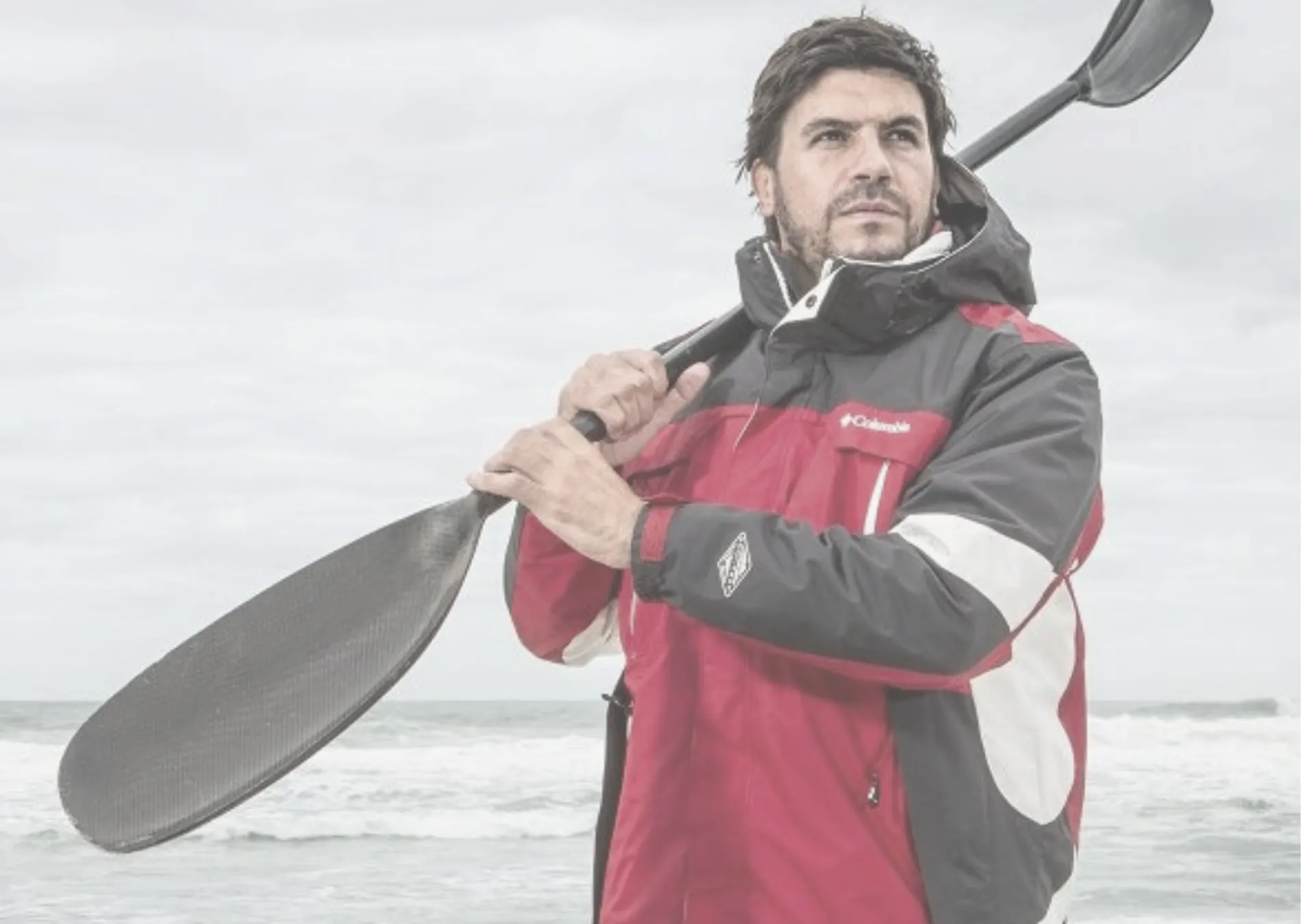Riaan Manser, explorer and founder of Students in Antarctica, holding a paddle on a windswept beach