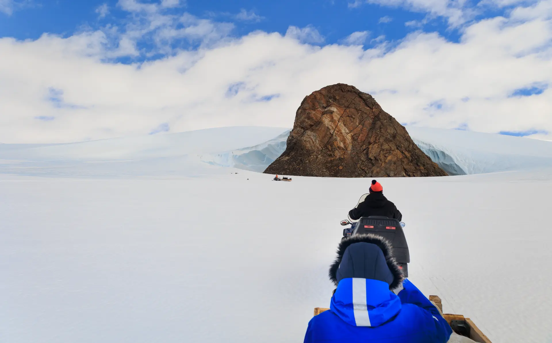 View from a sled behind a skidoo heading towards a rocky nunatak on the Antarctic ice