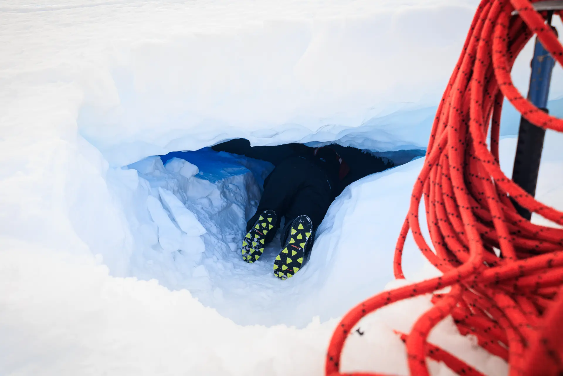 A team member descending into a crevasse beside a coiled red climbing rope