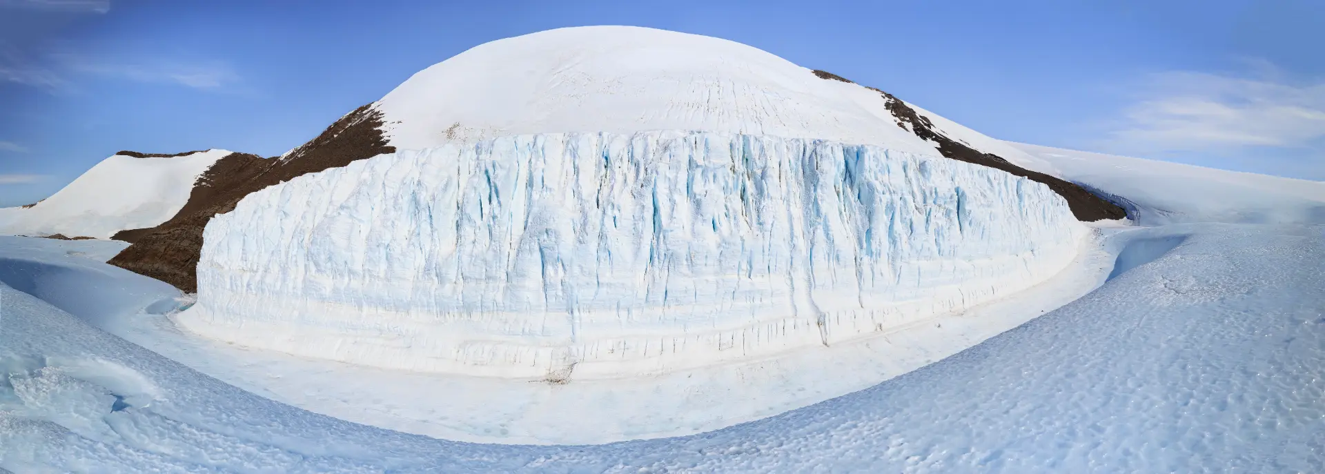 A towering blue glacier wall beneath a snow capped dome in Antarctica