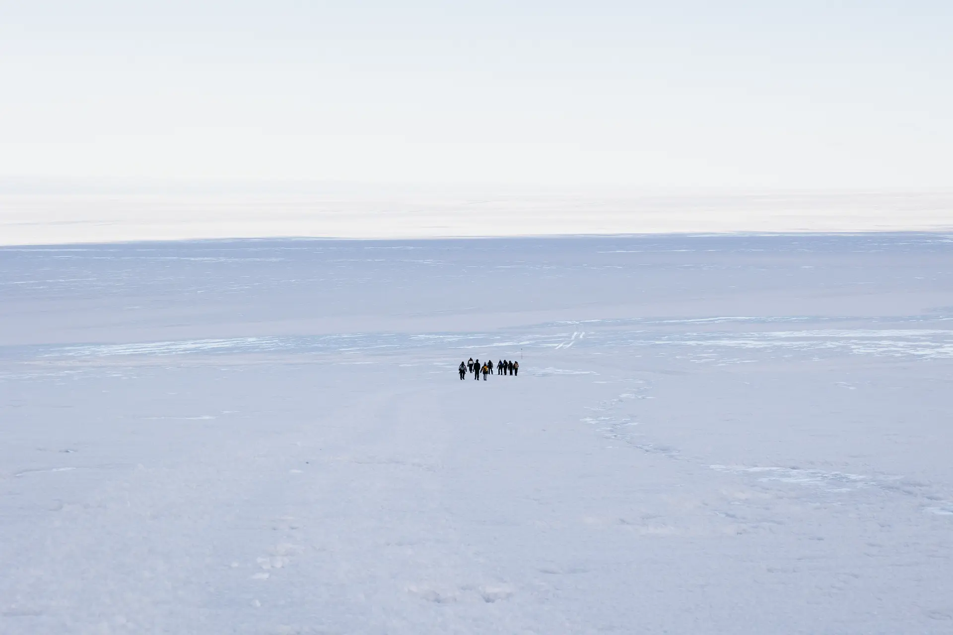 The expedition team walking as tiny figures across a vast white Antarctic ice plain