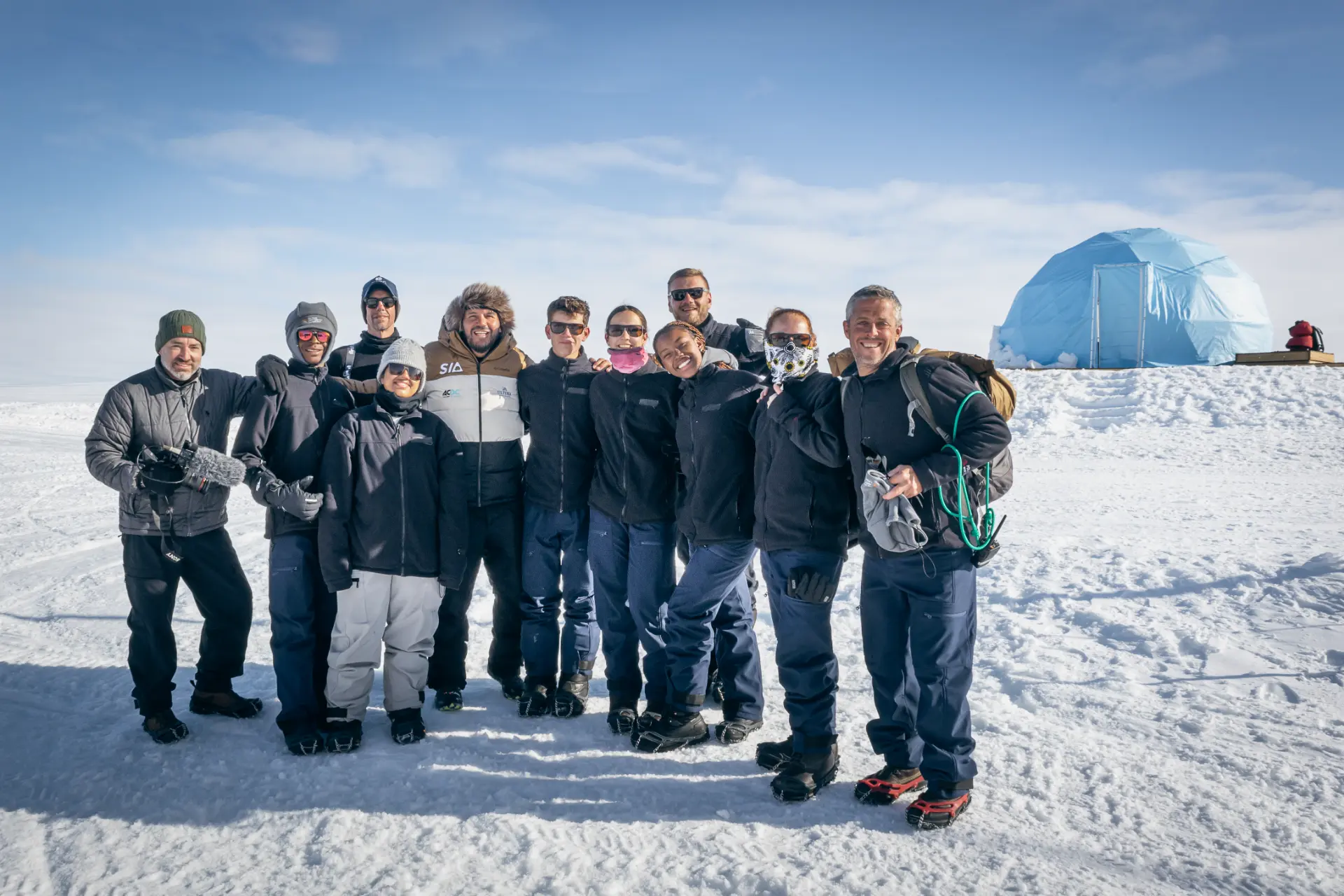 The full expedition team posing together on the snow in front of the Ultima Base dome